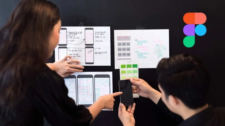 Dos diseñadores colaboran revisando wireframes impresos sobre una pared negra, discutiendo esquemas de una app móvil con colores y estructuras. El logo de Figma aparece en la esquina superior derecha.