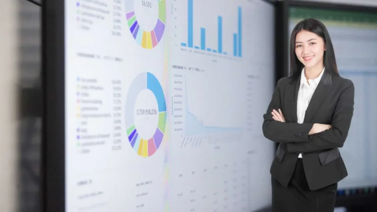 Mujer profesional sonriendo frente a una pantalla con gráficos de análisis de datos y diagramas circulares.